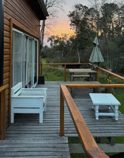 El deck de una cabaña al atardecer, con dos sillones y una mesa